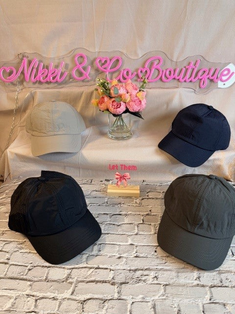 Four baseball caps on a stone surface with 'Nikki & Co Boutique' sign in the background.