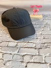 Black cap on a textured surface with 'Let Them' text and pink bow in the background.