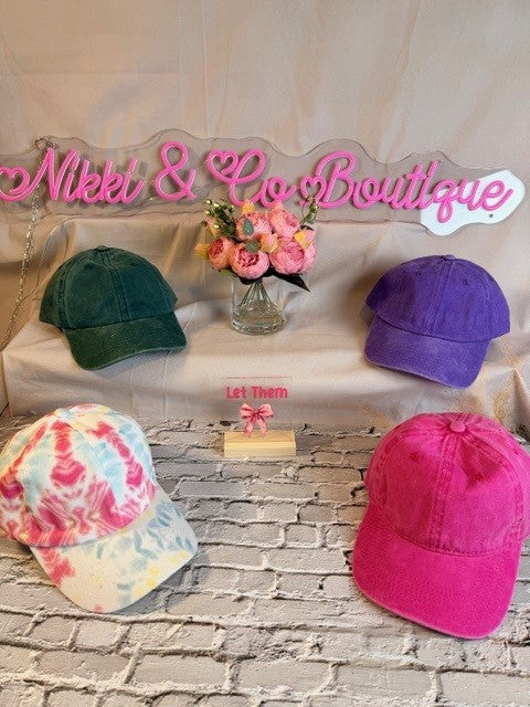 Colorful baseball caps on a stone surface with 'Nikki & Co Boutique' sign in the background.