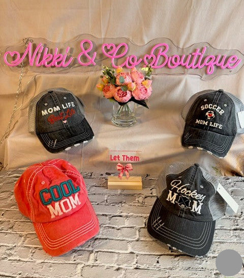 Collection of caps with text and floral arrangement on a neutral background with 'Nikki & Co Boutique' sign.