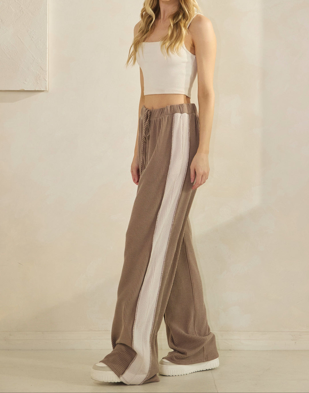 Woman wearing taupe ribbed pants with a cream-colored strip down the sides and matching top