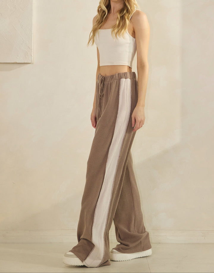 Woman wearing taupe ribbed pants with a cream-colored strip down the sides and matching top