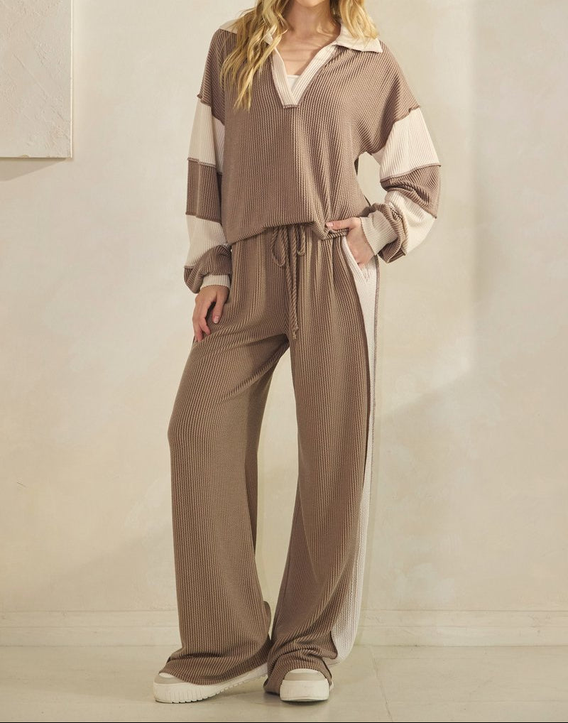Woman wearing taupe ribbed pants with a cream-colored strip down the sides and matching top