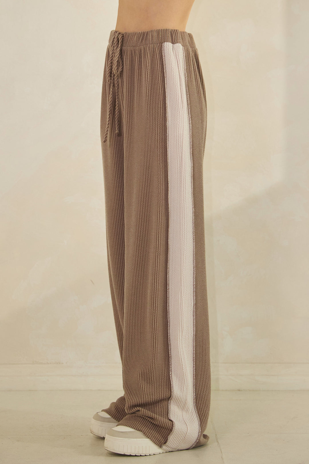 Woman wearing taupe ribbed pants with a cream-colored strip down the sides