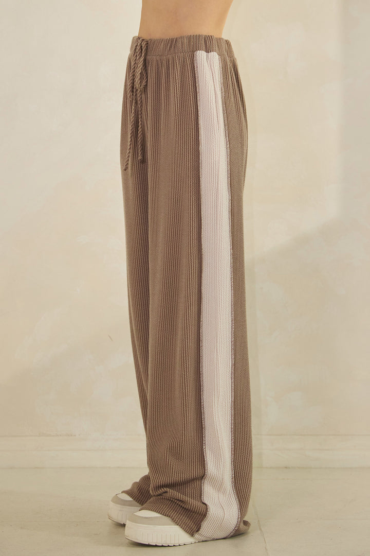 Woman wearing taupe ribbed pants with a cream-colored strip down the sides