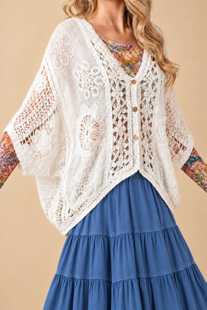 Woman wearing a mesh shirt layered under  floral crochet cardigan with a flowy skirt.
